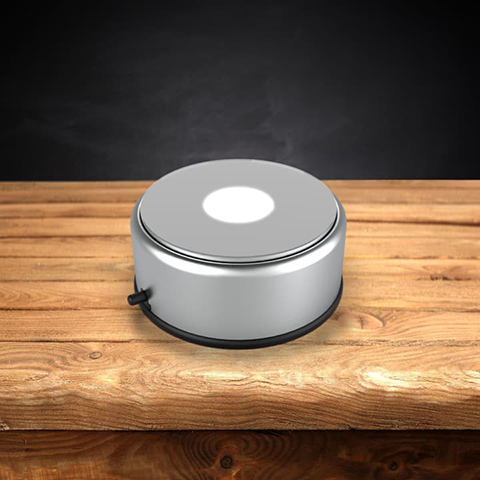 Round silver rotating LED light base on a wooden table.